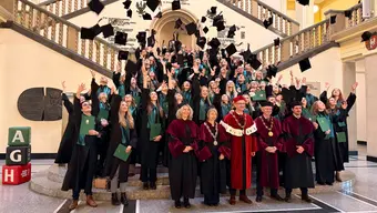 grupa ludzi ubrana w togi i birety pozują na schodach do pamiątkowego zdjęcia